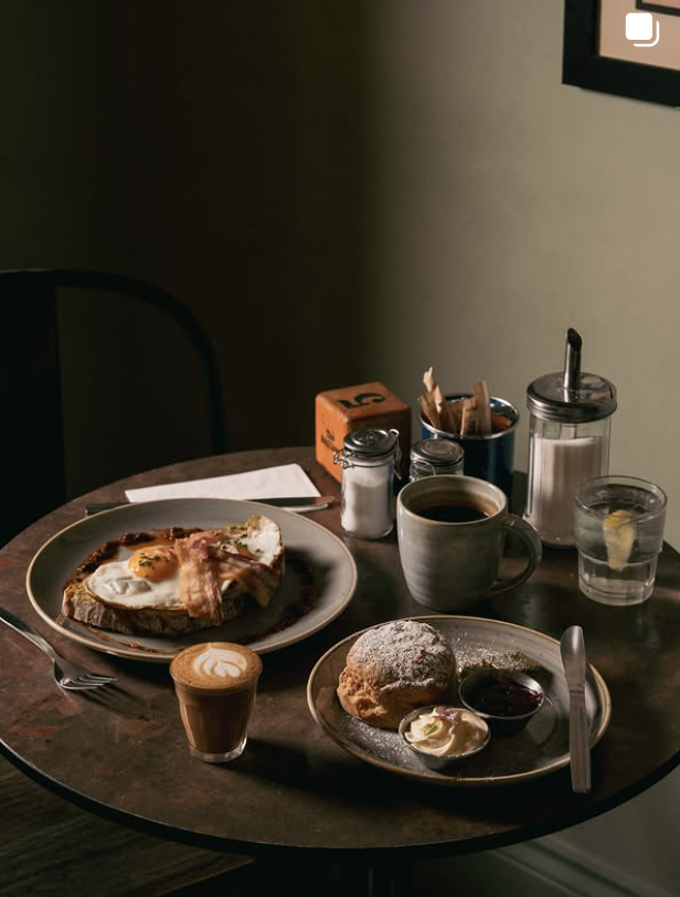 Breakfast plate with eggs on toast, scone with cream and jam, and a latte